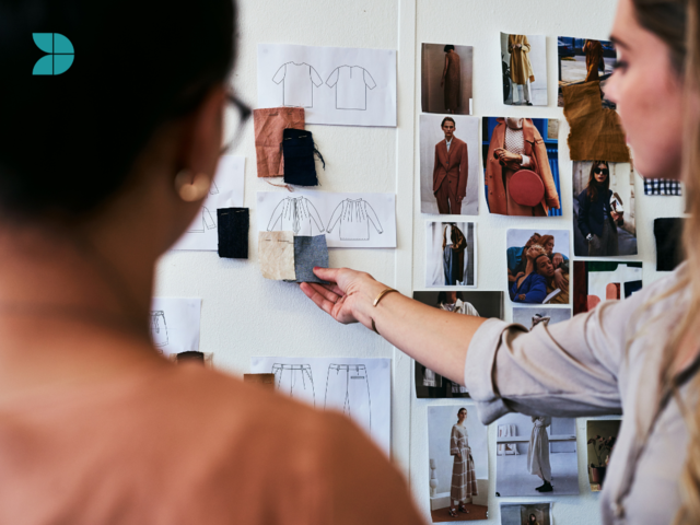 Two fashion designers looking at fashion sketches, and fabric samples.